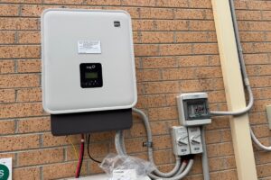 Fox ESS hybrid inverter and DC isolators installed on a brick wall at a Melbourne home by E3 Energy, with the top of the battery enclosure below