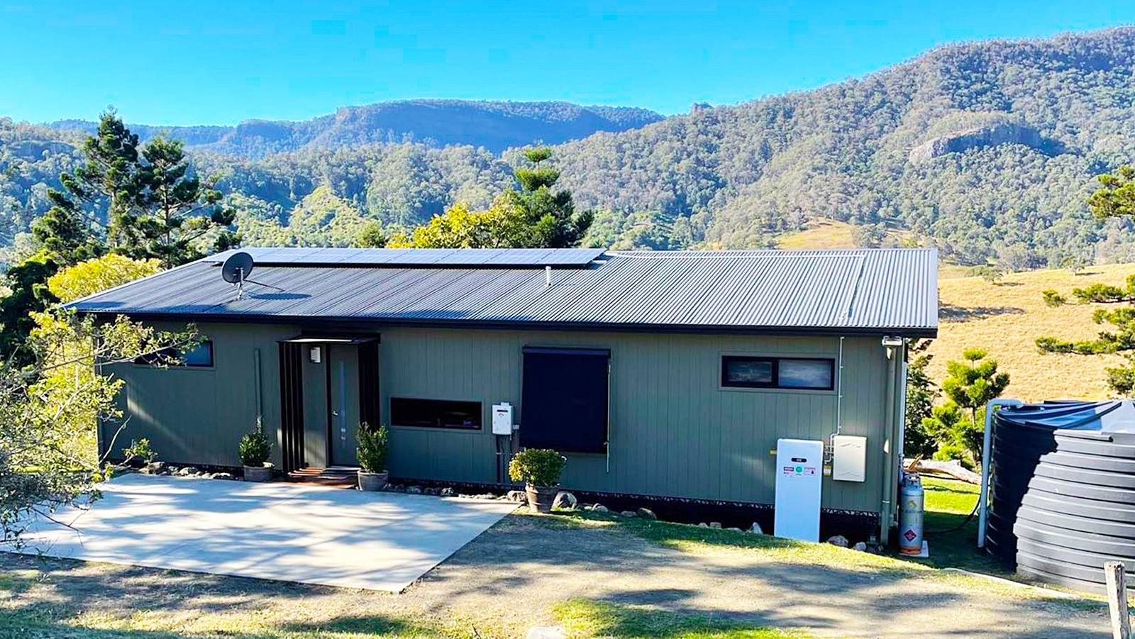 A SOFAR PowerAll battery mounted on the outside wall of an Australian house with solar panels on the roof and hills behind